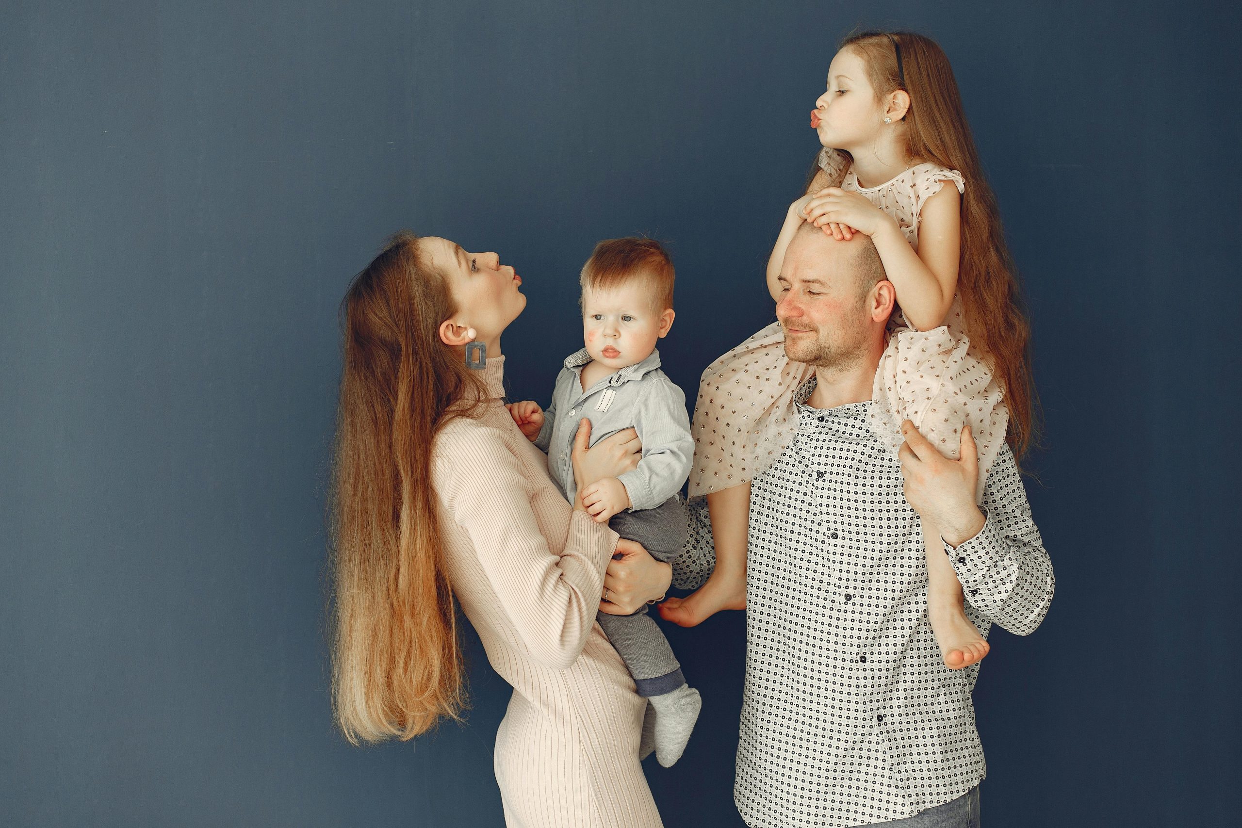 Portrait of a joyful family with parents and kids showing love and affection against a blue background.